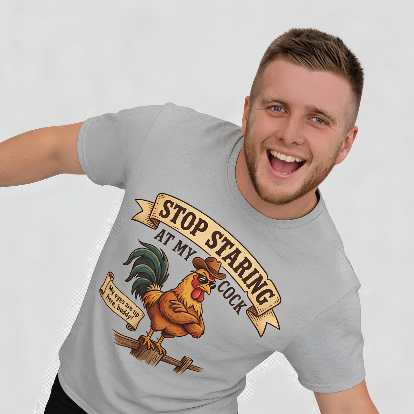 A smiling man models the gray Stop Staring at My Cock Tee featuring a bold rooster graphic and cheeky slogan, perfect for stag parties. The shirt stands out against a light, simple background.