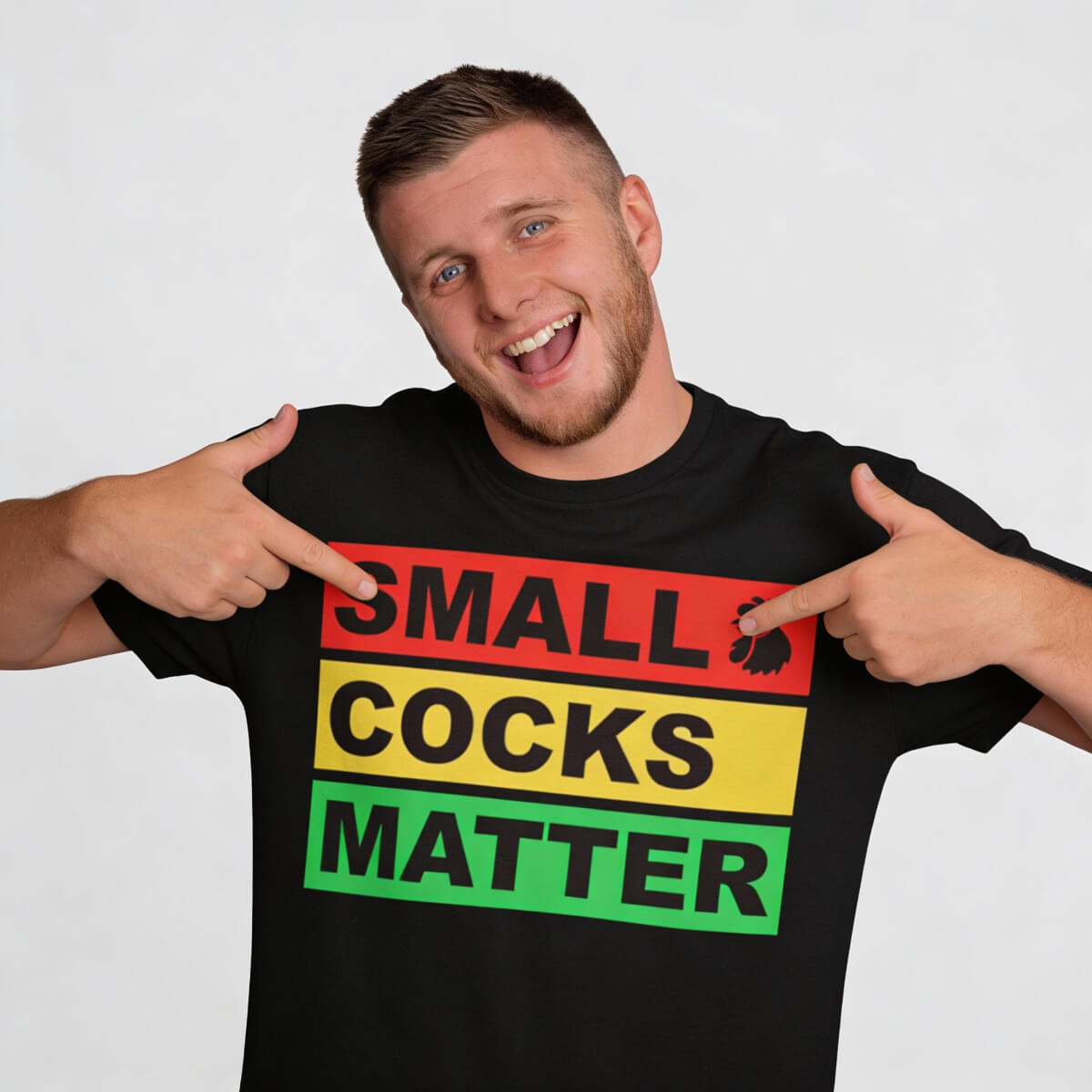 A smiling man points to his black Small Cocks Matter Tee, featuring "SMALL COCKS MATTER" in bold red, yellow, and green letters—a funny group shirt ideal for any stag do t-shirt collection.
