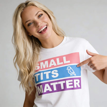 A smiling woman with long blonde hair points to her white Small Tits Matter Tee, showing off its colorful design and small bird illustration—perfect as a fun hen do t-shirt.