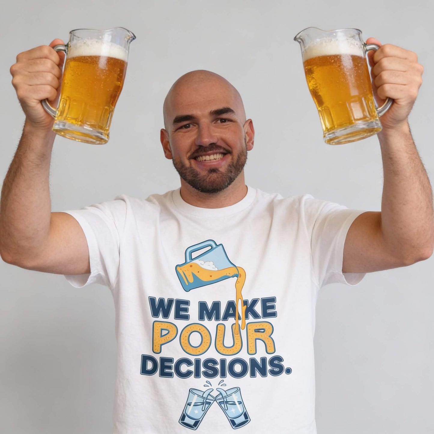 A smiling man holds two beers and wears the "We Make Pour Decisions Tee" featuring a spilling beer graphic—perfect for stag dos or pub crawls.