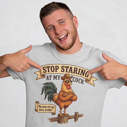 A smiling man points at his Stop Staring at My Cock Stag Do Tee, which features a cartoon rooster in a cowboy hat and the funny text, "Stop staring at my cock. My eyes are up here, buddy!"—perfect for stag parties or as a groom gag shirt.