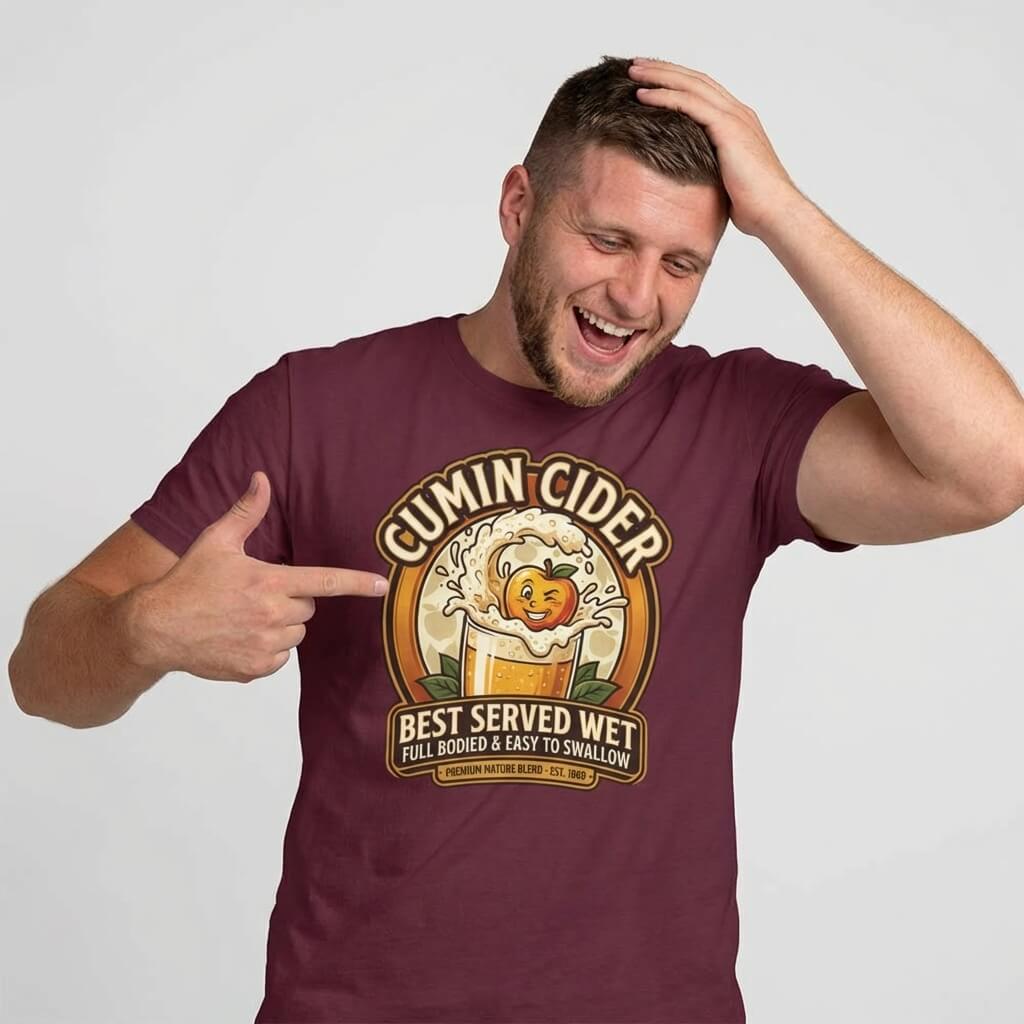 A smiling man in a Cumin Cider Stag Do Tee points at its cartoon apple-in-mug design with the text: “Cumin Cider: Best Served Wet. Full Bodied & Easy to Swallow.”.