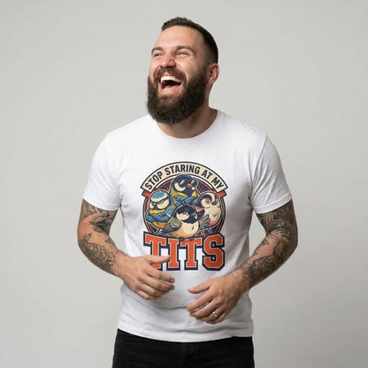 A bearded, tattooed man laughs while wearing the “Stop Staring at My Tits” Stag Do Tee, which features illustrated birds and a bold slogan. Set against a plain light gray background—it’s a perfect funny stag do outfit or unique groom gift.