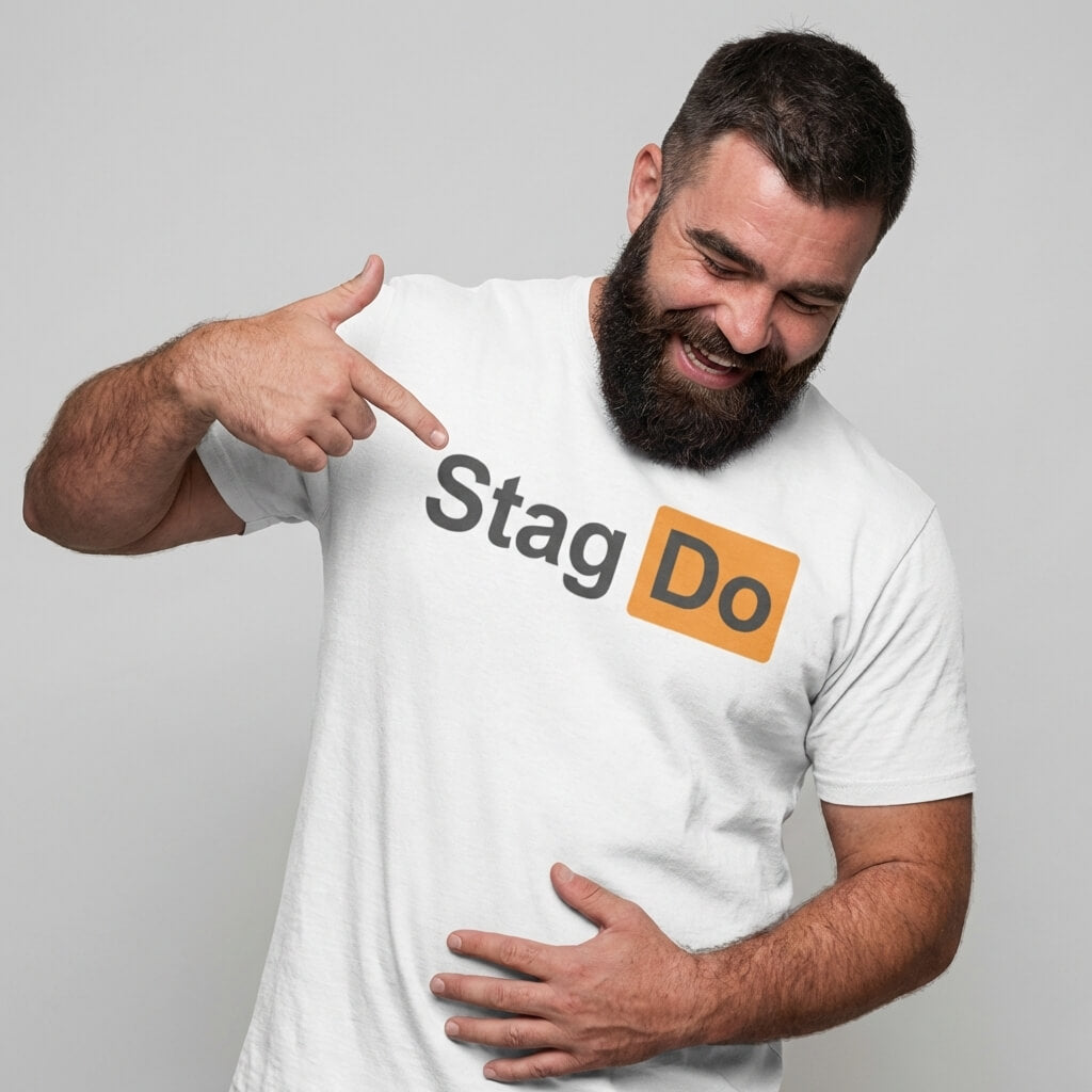 A bearded man smiles and points to his white Stag Do PornHub Tee, which features "Stag Do" with "Do" highlighted in an orange box, standing against a plain gray background.