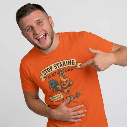 A smiling man in an orange Stop Staring at My Cock Stag Do Tee points at its cartoon rooster and witty text—an ideal funny groom or stag party shirt with a humorous design.
