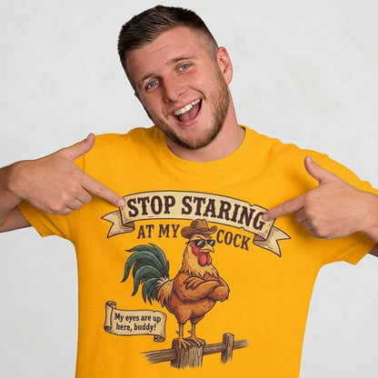 A smiling man points at his yellow Stop Staring at My Cock Stag Do Tee, which features a cartoon rooster and the phrase “My eyes are up here, buddy!” This funny t-shirt is ideal for laughs at any bachelor or stag party. The background is plain and light-colored.