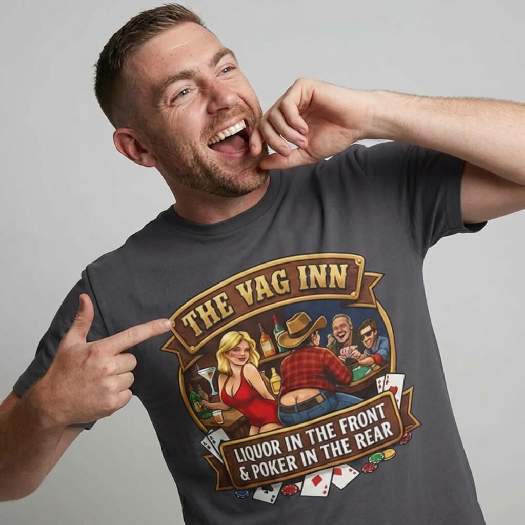 A smiling man points to his gray The Vag Inn Stag Do Tee, featuring cartoon figures playing cards and drinking. The shirt reads, “The Vag Inn: Liquor in the Front & Poker in the Rear”—a hilarious bachelor party pick!.