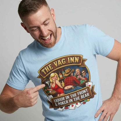 A man points at his light blue The Vag Inn Stag Do Tee, featuring playful cartoon characters, playing cards, and the text "THE VAG INN. LIQUOR IN THE FRONT & POKER IN THE REAR"—a funny bachelor party shirt.
