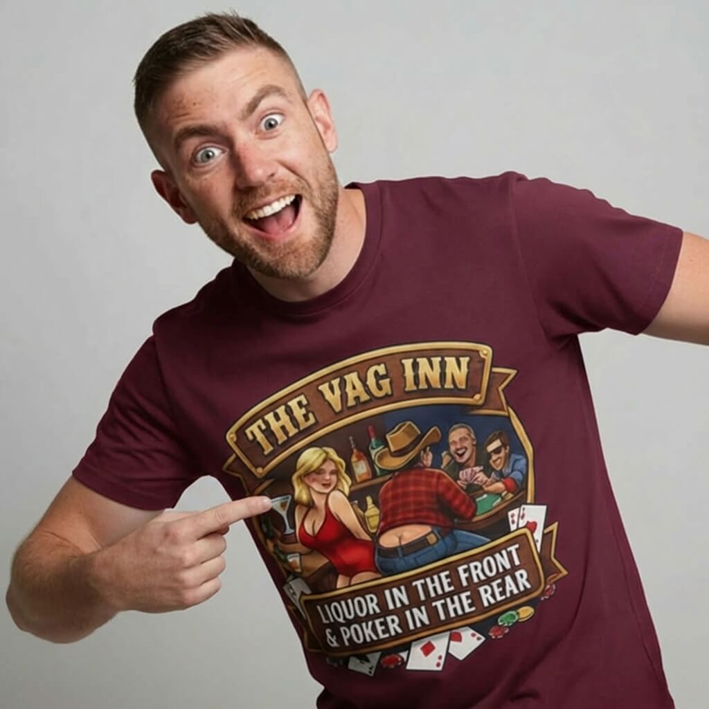 A cheerful man with short hair and a beard grins, pointing at his maroon 'The Vag Inn Stag Do Tee' featuring a colorful cartoon bar scene and the slogan: "Liquor in the front & poker in the rear.