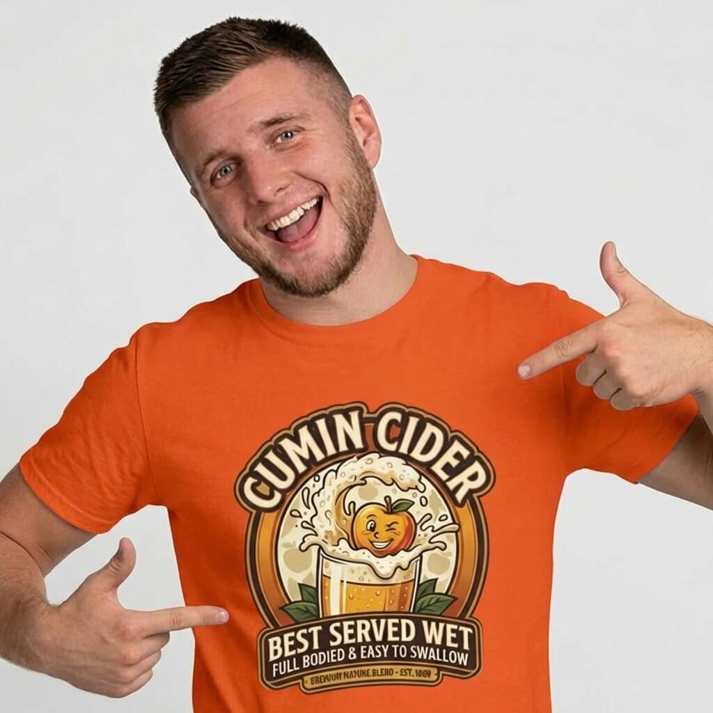 A man grins, pointing at his bright orange Cumin Cider Stag Do Tee featuring a cartoon cider glass and the slogan “Best Served Wet, Full Bodied & Easy to Swallow.” A hilarious groom gift or stag do shirt that guarantees laughs!.