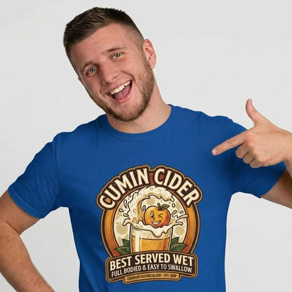 A man in a blue shirt points at himself wearing the Cumin Cider Stag Do Tee. This funny shirt shows a cartoon cider glass with "Cumin Cider. Best Served Wet. Full Bodied & Easy to Swallow"—perfect for groom gifts!.