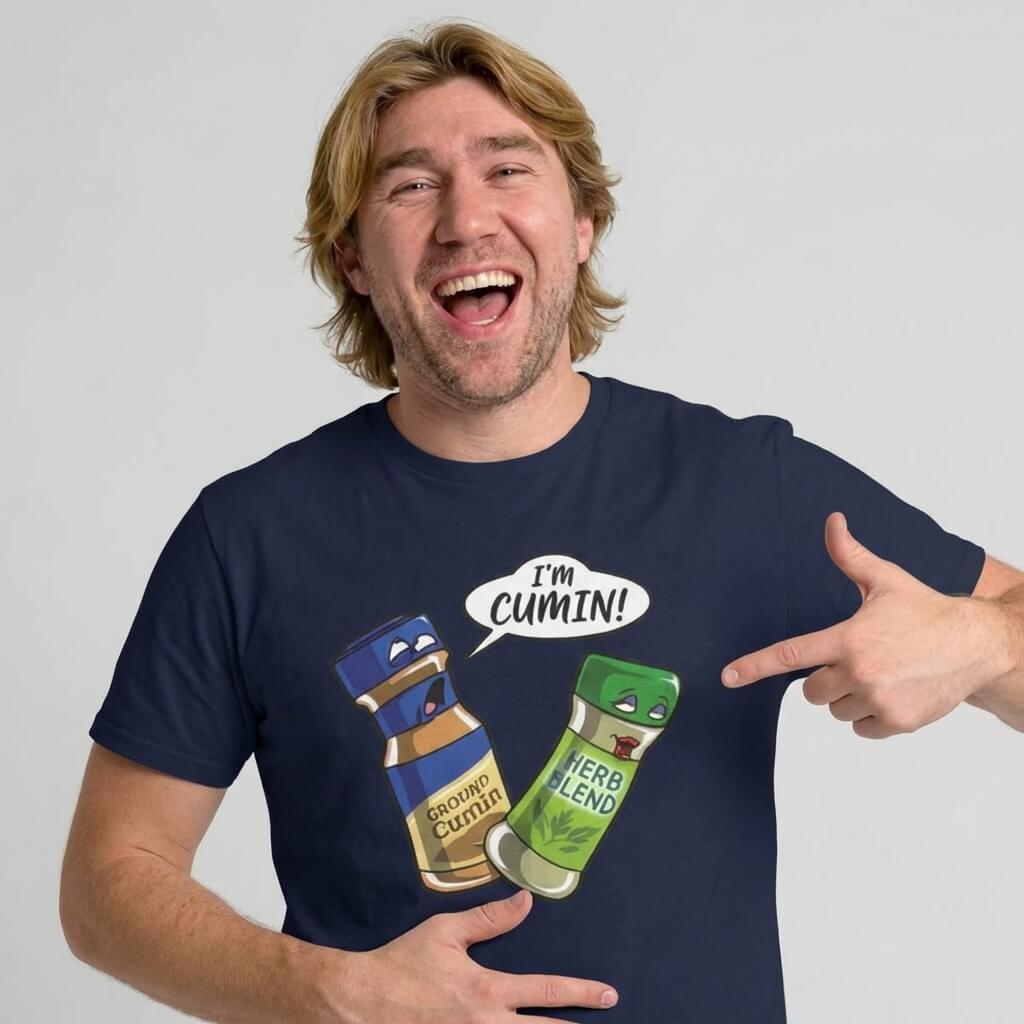 A blonde man smiles and points at his navy "I’m Cumin!" Stag Do Tee, featuring cartoon spice jars—one shouting "I’m Cumin!" at a shocked Herb Blend—making it the perfect funny shirt for stag parties.