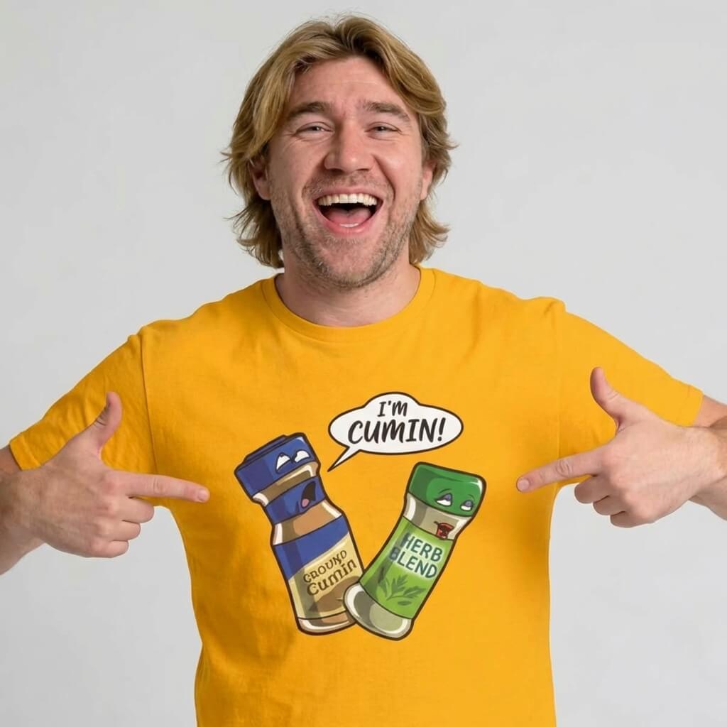 A smiling man points to his "I’m Cumin!" Stag Do Tee, featuring cartoon spice jars—one labeled Ground Cumin with the phrase I’m cumin! jokingly addressing a Herb Blend jar, both drawn with expressive faces.