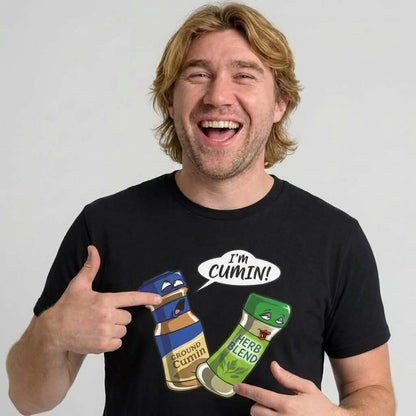 A smiling man points to his black “I’m Cumin!” Stag Do Tee, which features cartoon spice jars labeled Ground Cumin (saying IM CUMIN!) and Herb Blend with expressive faces—a funny tee perfect for stag dos.