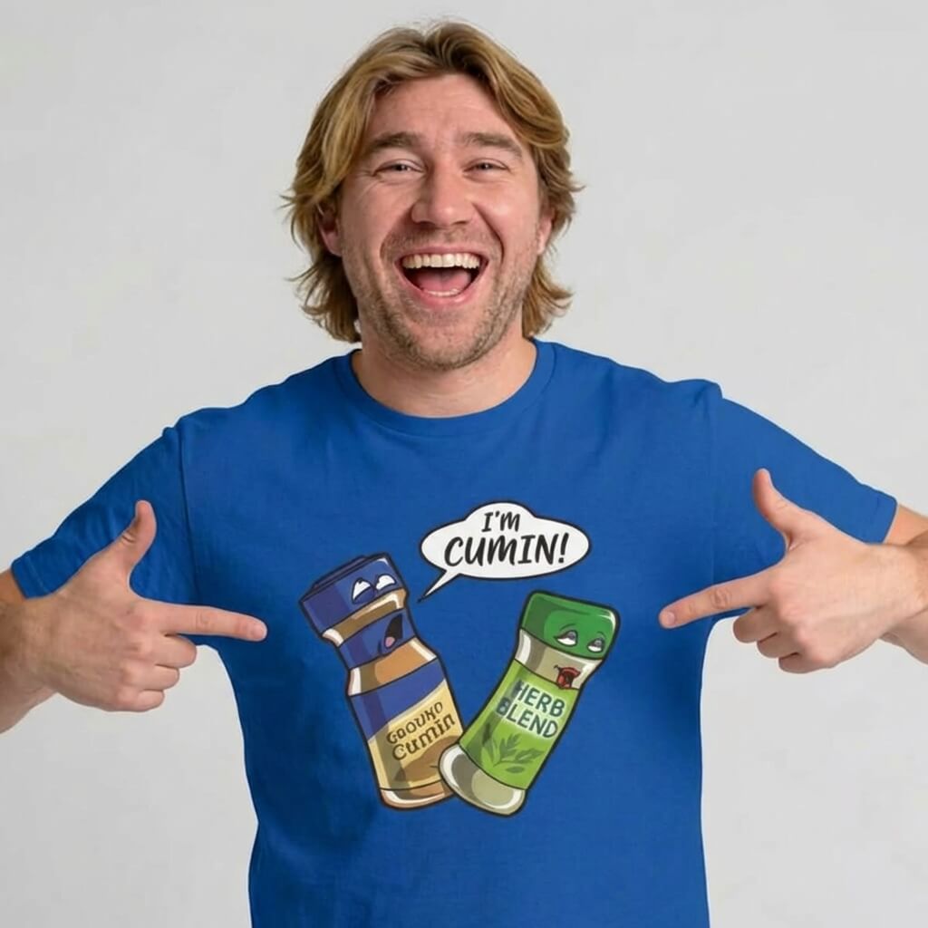 A smiling man in a blue "I’m Cumin!" Stag Do Tee points at his shirt, which features cartoon spice jars—Ground Cumin saying "Im cumin!" to Herb Blend. Both jars have expressive faces—a hilarious stag do shirt.
