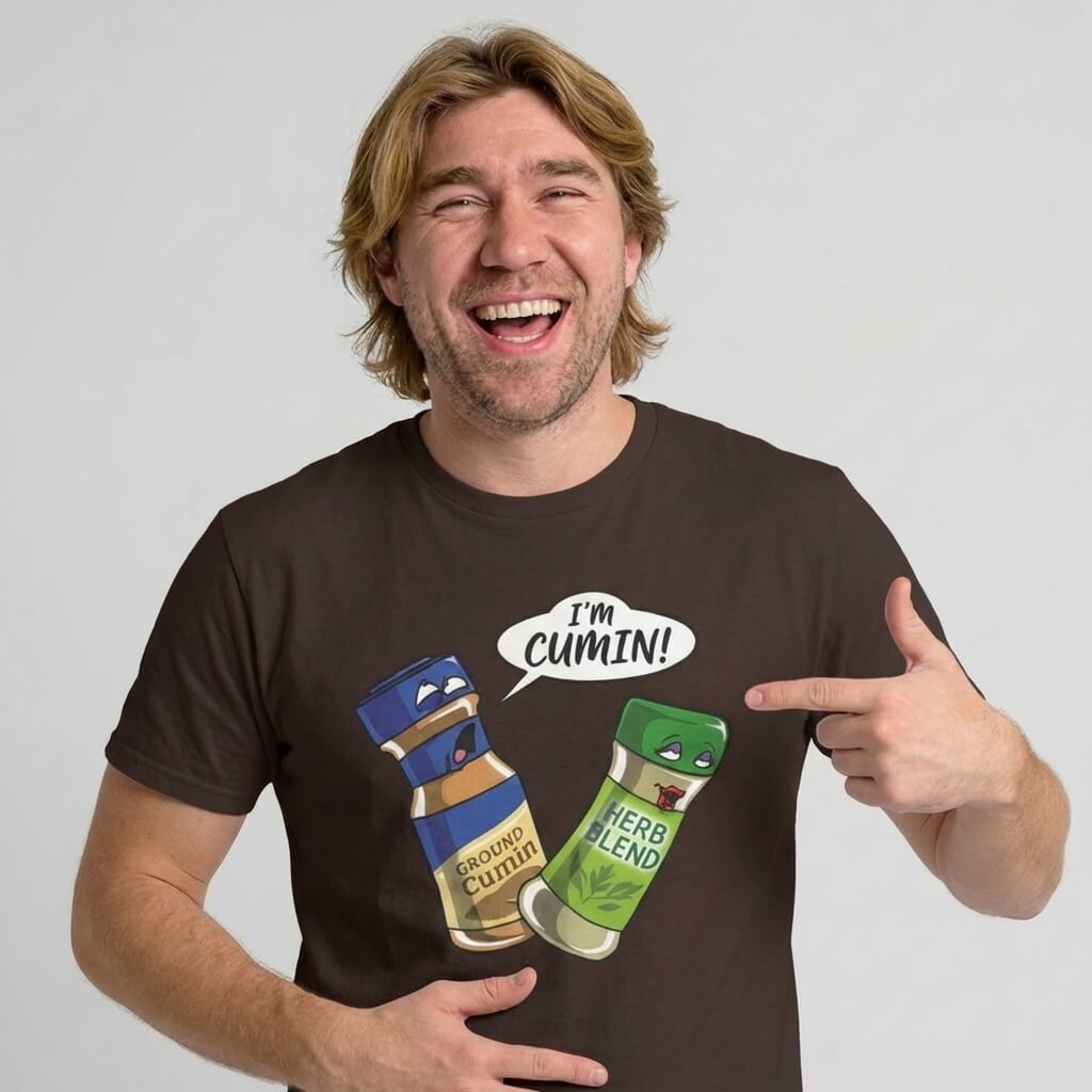 A smiling blond man points to his "I’m Cumin!" Stag Do Tee, featuring cartoon spice jars—one shocked jar labeled Ground Cumin and another saying "I’m Cumin!" in a speech bubble—a hilarious choice for stag dos.