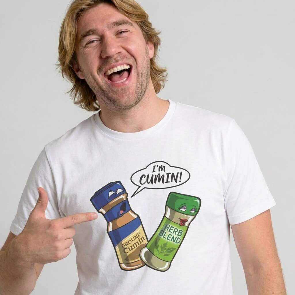 A smiling man with light brown hair points to his “I’m Cumin!” Stag Do Tee, featuring cartoon spice bottles—one labeled Ground Cumin saying "I'm cumin!" to another labeled Herb Blend, both with expressive faces.