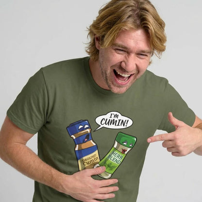 A laughing man wears the "I’m Cumin!" Stag Do Tee—an olive green shirt with cartoon spice bottles. One bottle, Ground Cumin, looks shocked as Herb Blend exclaims “IM CUMIN!”—the perfect funny stag do shirt.