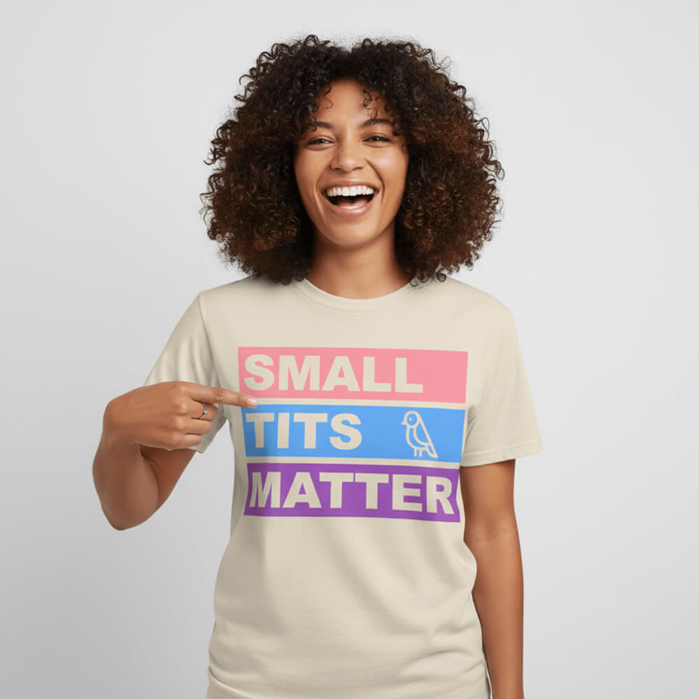 A smiling person with curly hair points to the "Small Tits Matter" Tee, featuring colorful block letters and a playful bird illustration next to the word TITS.