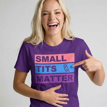 A smiling woman in a purple "Small Tits Matter" Tee points to the bold text on her shirt while holding her stomach—a cheeky choice for playful party vibes.