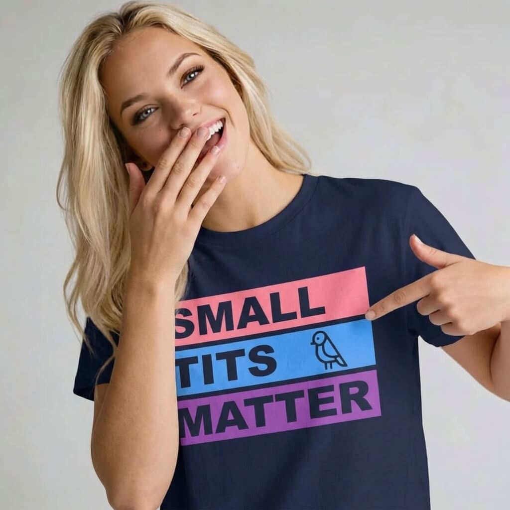 A smiling woman with long blonde hair covers her mouth and points to her "Small Tits Matter" Tee, a navy blue shirt with bold colored blocks and a small bird drawing next to the word TITS.