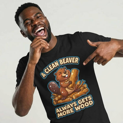 A grinning man points to his "A Clean Beaver Always Gets More Wood" Stag Do Tee, featuring a cartoon beaver on logs and the cheeky slogan—ideal for anyone seeking a funny stag do shirt.