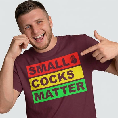 A smiling man in a maroon Small Cocks Matter Stag Do Tee with vibrant block letters and a rooster illustration points at the text—a hilarious bachelor party shirt for any stag do collection.