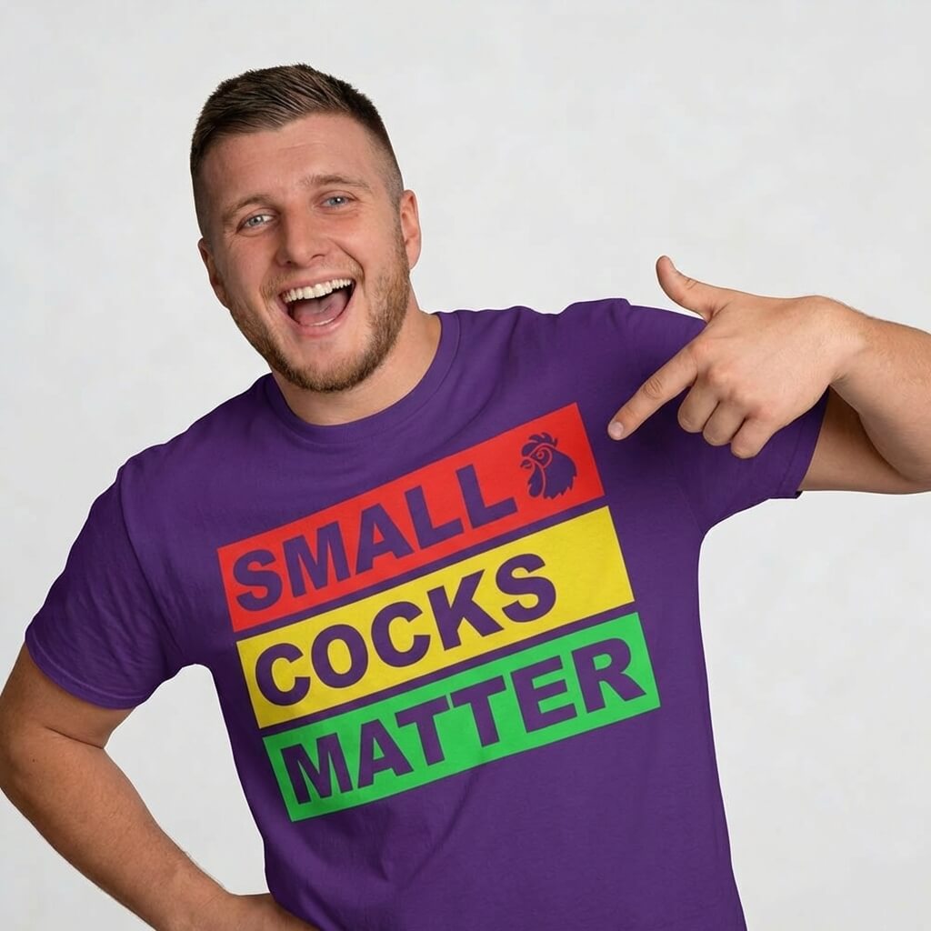 A smiling man in the Small Cocks Matter Stag Do Tee, featuring colorful text and a rooster, points at his shirt—a hilarious choice for bachelor parties or stag dos that’s sure to get laughs.