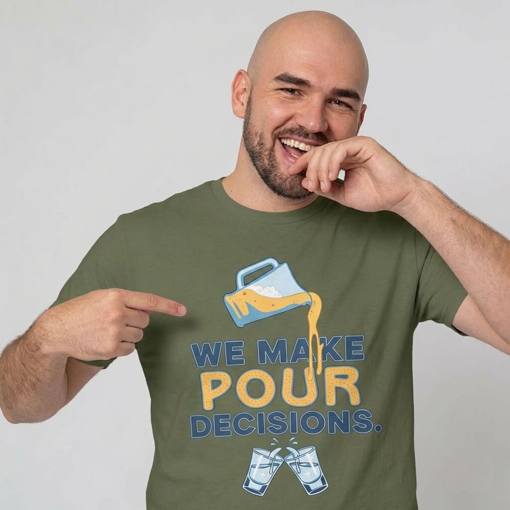 A smiling bald man points to his “We Make Pour Decisions Stag Do Tee,” an olive green shirt featuring a beer pitcher pouring into clinking glasses and the witty slogan, “We make pour decisions.”.