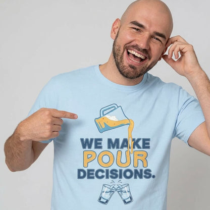 A smiling bald man with a beard points at his light blue We Make Pour Decisions Stag Do Tee, featuring a beer being poured and clinking glasses. He touches his ear, looking ready for an epic night out.