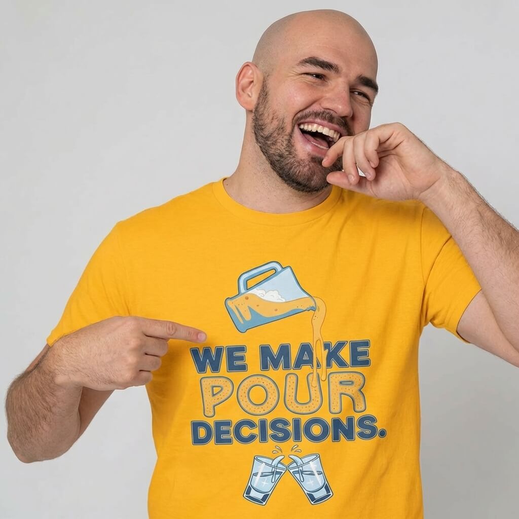 A smiling bearded bald man wears the yellow "We Make Pour Decisions Stag Do Tee" featuring a spilling pitcher and clinking glasses. He points at the text on the shirt and playfully touches his mouth.