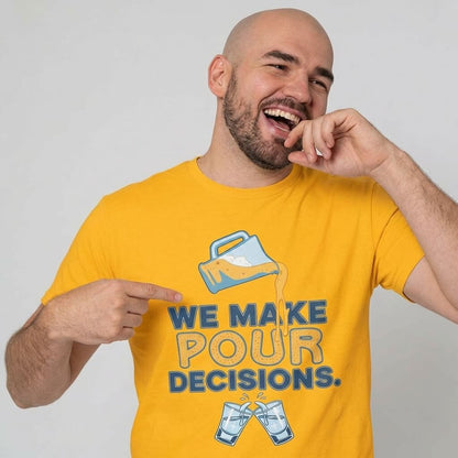A smiling bearded bald man wears the yellow "We Make Pour Decisions Stag Do Tee" featuring a spilling pitcher and clinking glasses. He points at the text on the shirt and playfully touches his mouth.