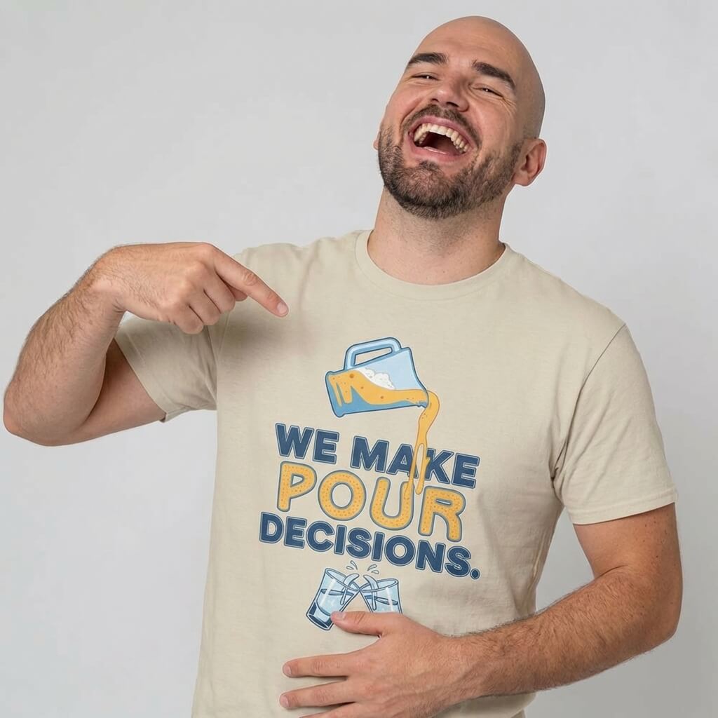 A bearded, bald man smiles and points at his "We Make Pour Decisions Stag Do Tee," featuring a cartoon jug pouring liquid. This fun design makes it the perfect shirt for any groom party, stag do, or pub crawl. He stands against a plain light background.
