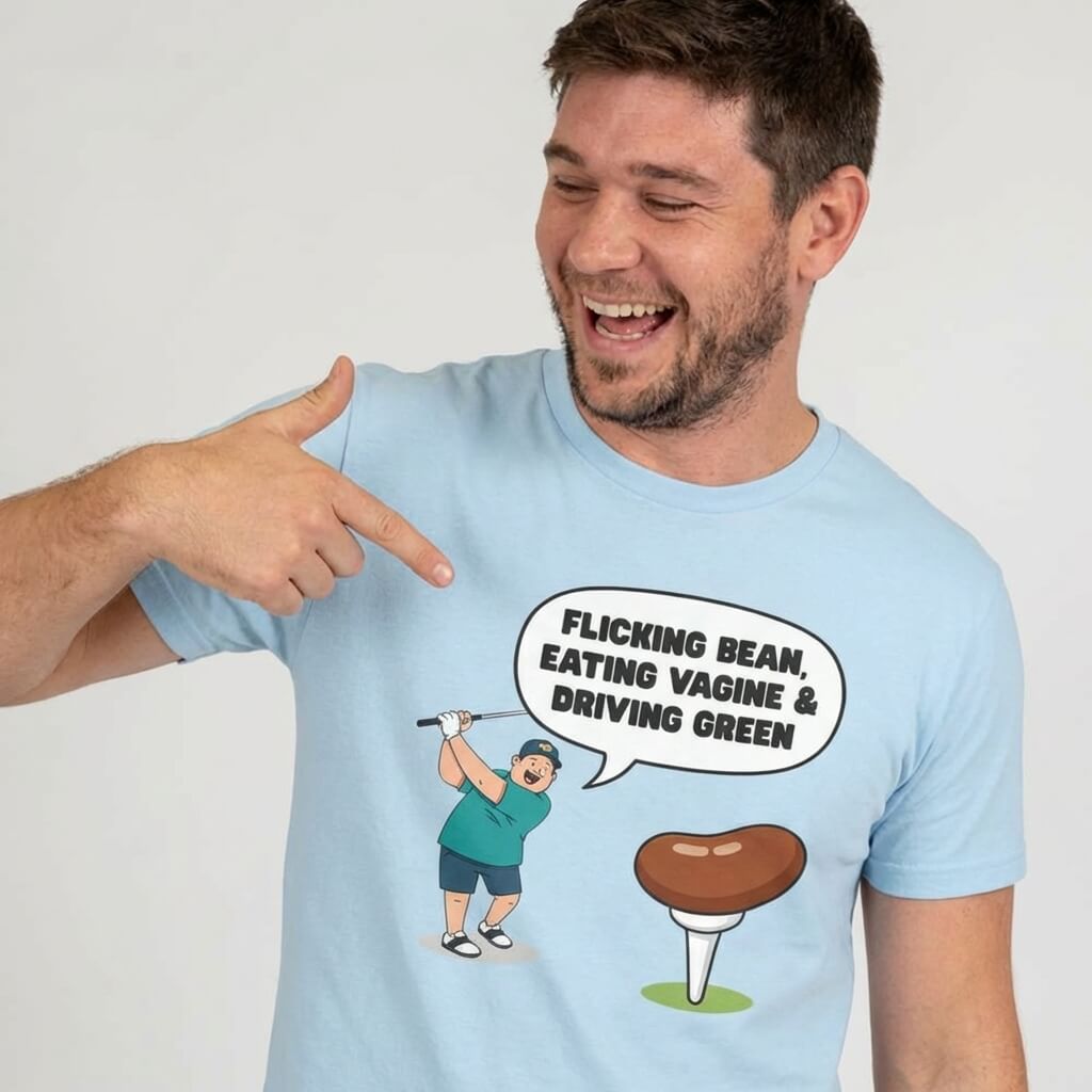 A smiling man points at his "Flicking Bean, Eating Vagine & Driving Green" Tee—a light blue shirt with a cartoon golfer and cheeky slogan, making it the perfect funny stag do golf t-shirt.