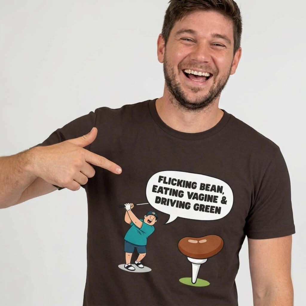 A smiling man points to his black "Flicking Bean, Eating Vagine & Driving Green" Tee, featuring a cartoon golfer and bean on a tee with the slogan in a speech bubble above the golfer.