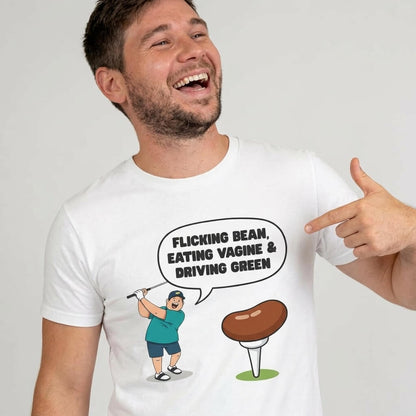 A smiling man points at his white "Flicking Bean, Eating Vagine & Driving Green" Tee, featuring a cartoon golfer and brown tee—a funny, rude golf t-shirt ideal for stag dos!.