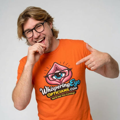 A smiling man with glasses and long hair points at his Whispering Eye Opticians Logo Tee, which features a cartoon eye inside pink lips and the slogan "We’ll See You Coming!.