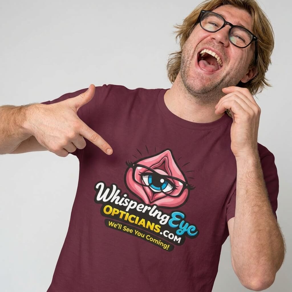 A smiling man in glasses points at his Whispering Eye Opticians Logo Tee (We'll See You Coming!), featuring a cartoon eye in lips. It's the perfect rude t-shirt for fun occasions and guaranteed to get laughs.