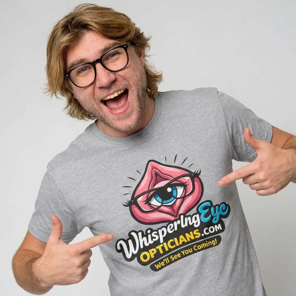 A smiling man with medium-length hair and glasses points at his gray Whispering Eye Opticians Logo Tee (We'll See You Coming!), featuring an illustrated eye within pink lips—perfect for a stag do t-shirt.