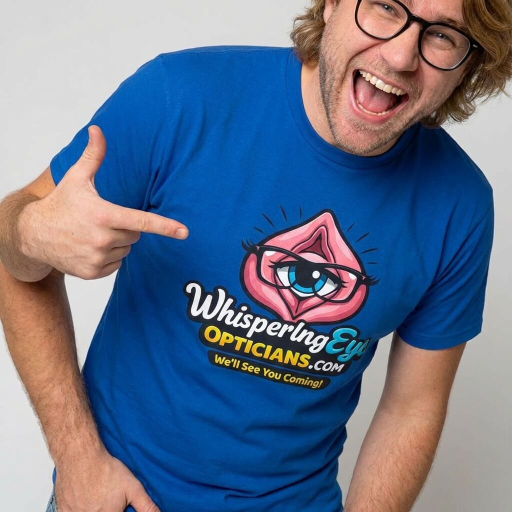 A smiling man with glasses points to his blue Whispering Eye Opticians Logo Tee, featuring a stylized eye in pink lips and the slogan “We’ll See You Coming!”.