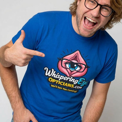 A smiling man with glasses points to his blue Whispering Eye Opticians Logo Tee, featuring a stylized eye in pink lips and the slogan “We’ll See You Coming!”.