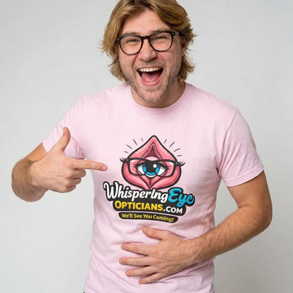 A smiling man with glasses and shaggy hair points at his light pink Whispering Eye Opticians Logo Tee (We'll See You Coming!)—the perfect cheeky shirt for a stag do or fun night out.