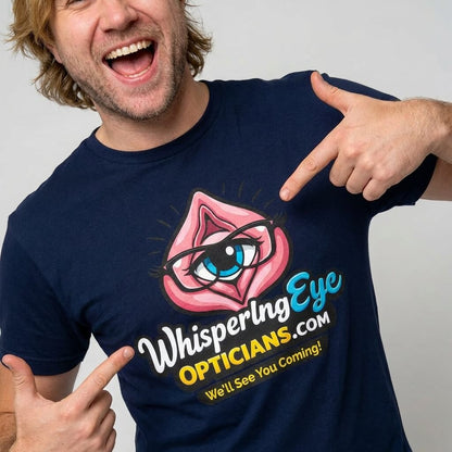 A smiling man points at his navy blue Whispering Eye Opticians Logo Tee (We'll See You Coming!), which features an eye graphic in a pink shape—a perfect cheeky, rude t-shirt for stag dos with a playful wink.