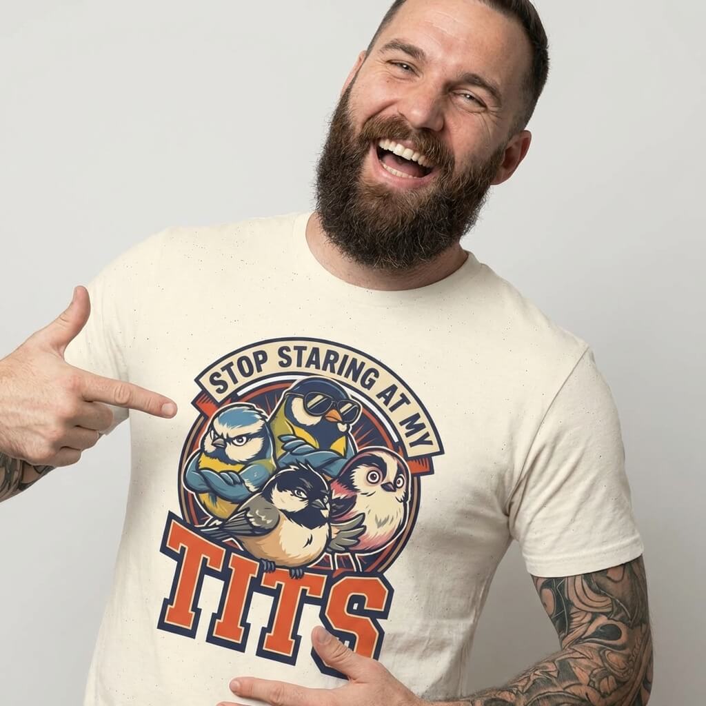 A tattooed, bearded man points at the “Stop Staring at My Tits” Stag Do Tee, featuring cartoon birds and humorous text—ideal for stag do outfits or as a unique gift for the groom.
