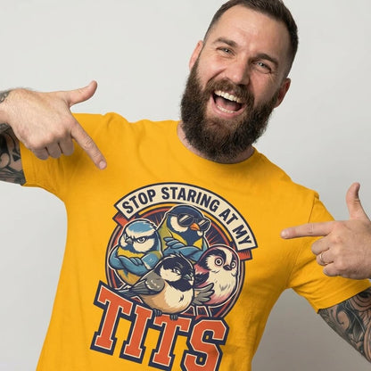 A bearded man with tattoos smiles and points at his yellow “Stop Staring at My Tits” Stag Do Tee, decorated with cartoon birds—an ideal funny choice for stag do outfits or a hilarious gift for the groom.
