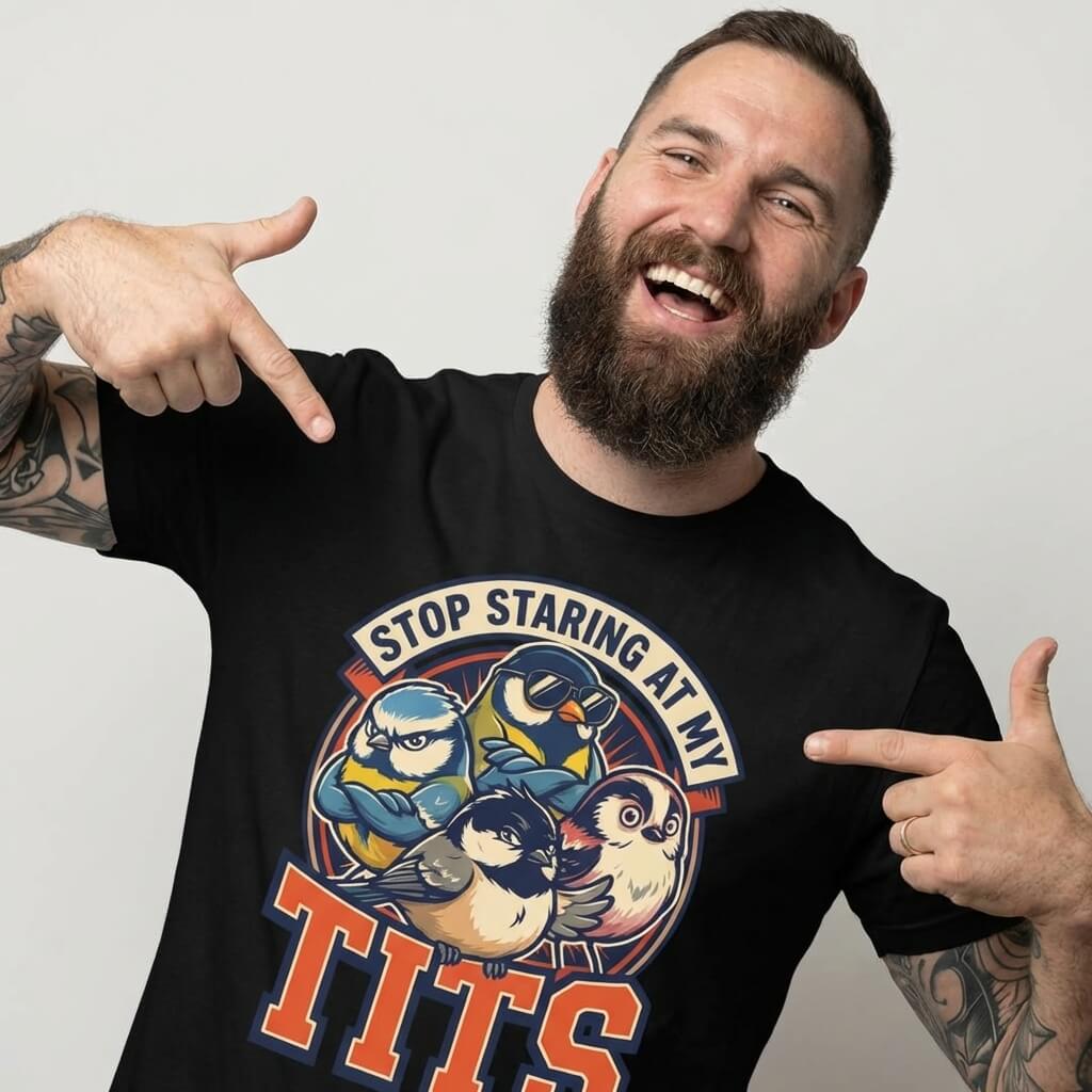 A bearded man with tattoos smiles and points at his “Stop Staring at My Tits” Stag Do Tee, featuring cartoon birds and bold text. This funny T-shirt makes a hilarious groom gift or stag do outfit for any bachelor party.