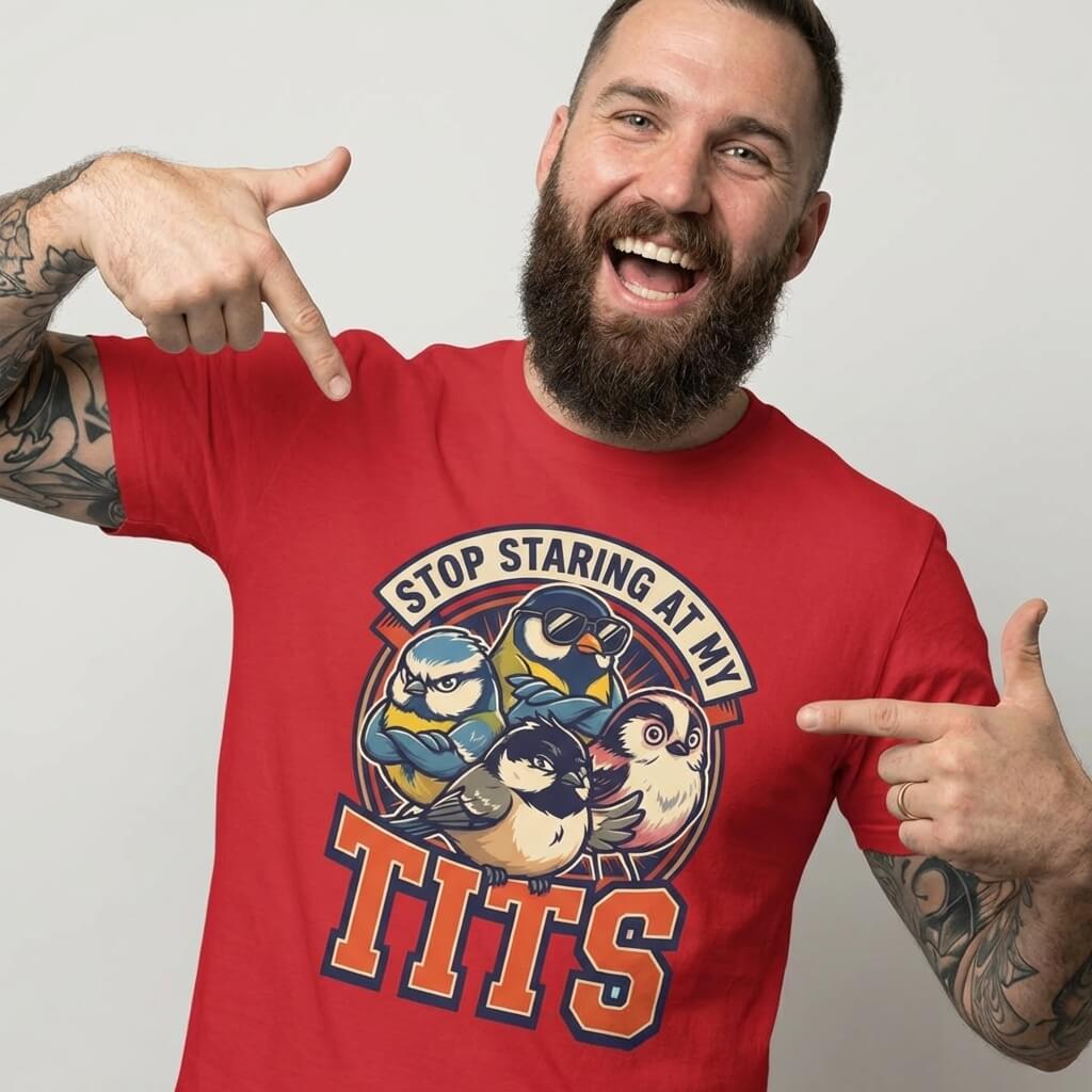 A bearded, tattooed man grins as he points at his “Stop Staring at My Tits” Stag Do Tee—featuring cartoon birds and bold text. This cheeky tee is perfect for funny stag do outfits or as a memorable gift for the groom.