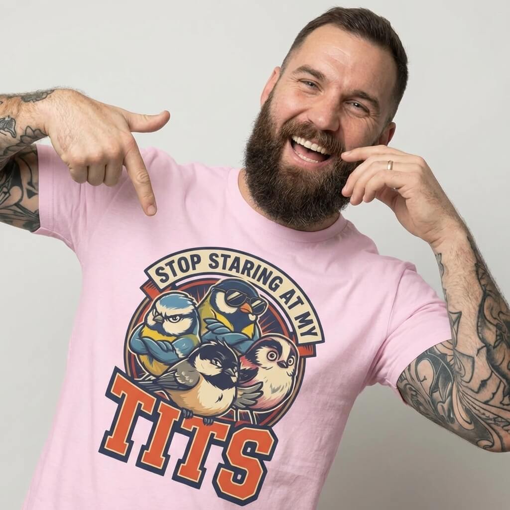 A bearded man in the “Stop Staring at My Tits” Stag Do Tee—featuring cartoon birds and bold text—smiles and points to his shirt. A hilarious stag do outfit or a unique groom gift!.