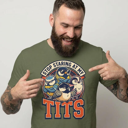 A tattooed, bearded man smiles and points at his green “Stop Staring at My Tits” Stag Do Tee, a hilarious shirt with cartoon birds—perfect for funny stag parties or as a groom gift.
