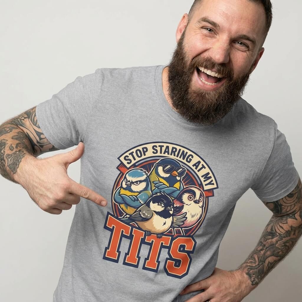 A bearded, tattooed man grins and points at his “Stop Staring at My Tits” Stag Do Tee, decorated with cartoon birds—an ideal pick for funny stag do outfits.
